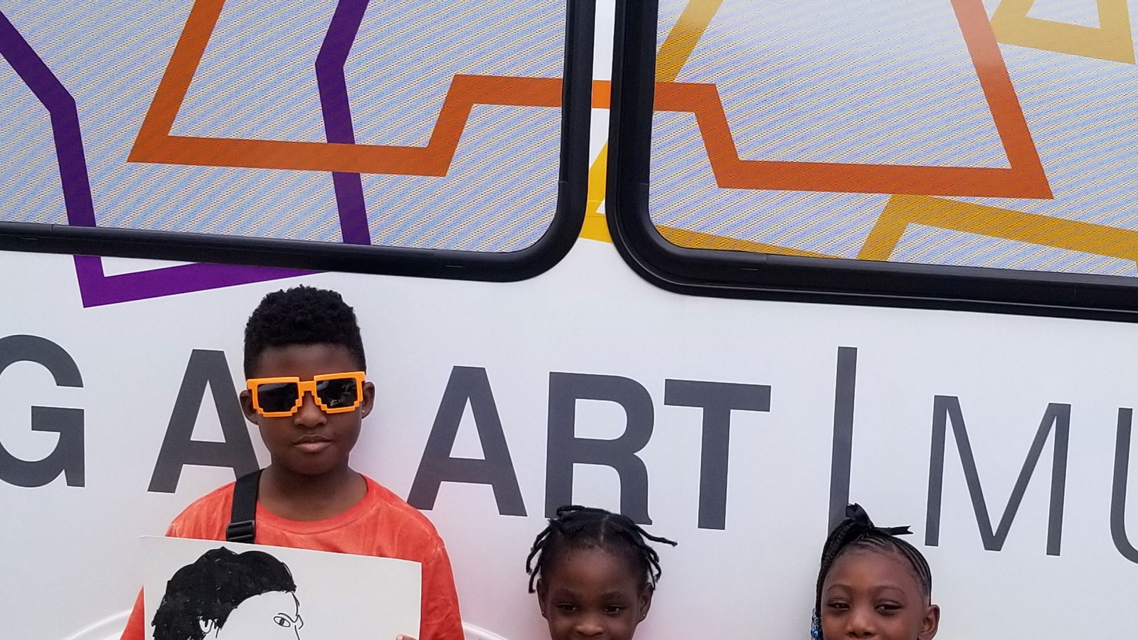 Children proudly holding up their colorful artwork in front of the Young At Art Museum mobile art bus in Plantation, Florida