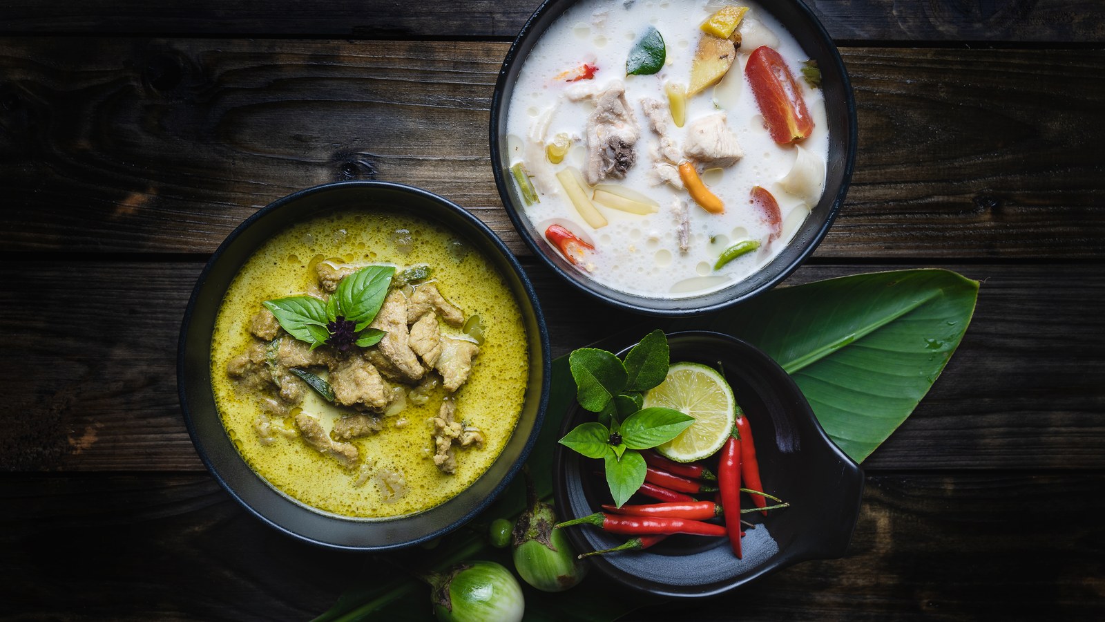 Bowls of Thai soup on a dark wooden table, with the Baitong Thai & Sushi Bar logo visible in the foreground