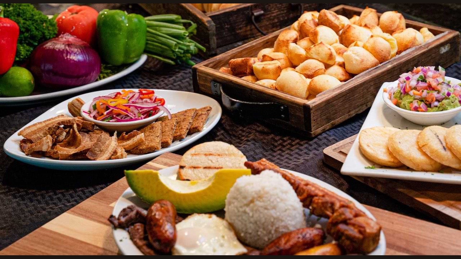 El Balcón de las Américas Colombian food spread — bandeja paisa with grilled meats, arepas, avocado, rice, and plantains